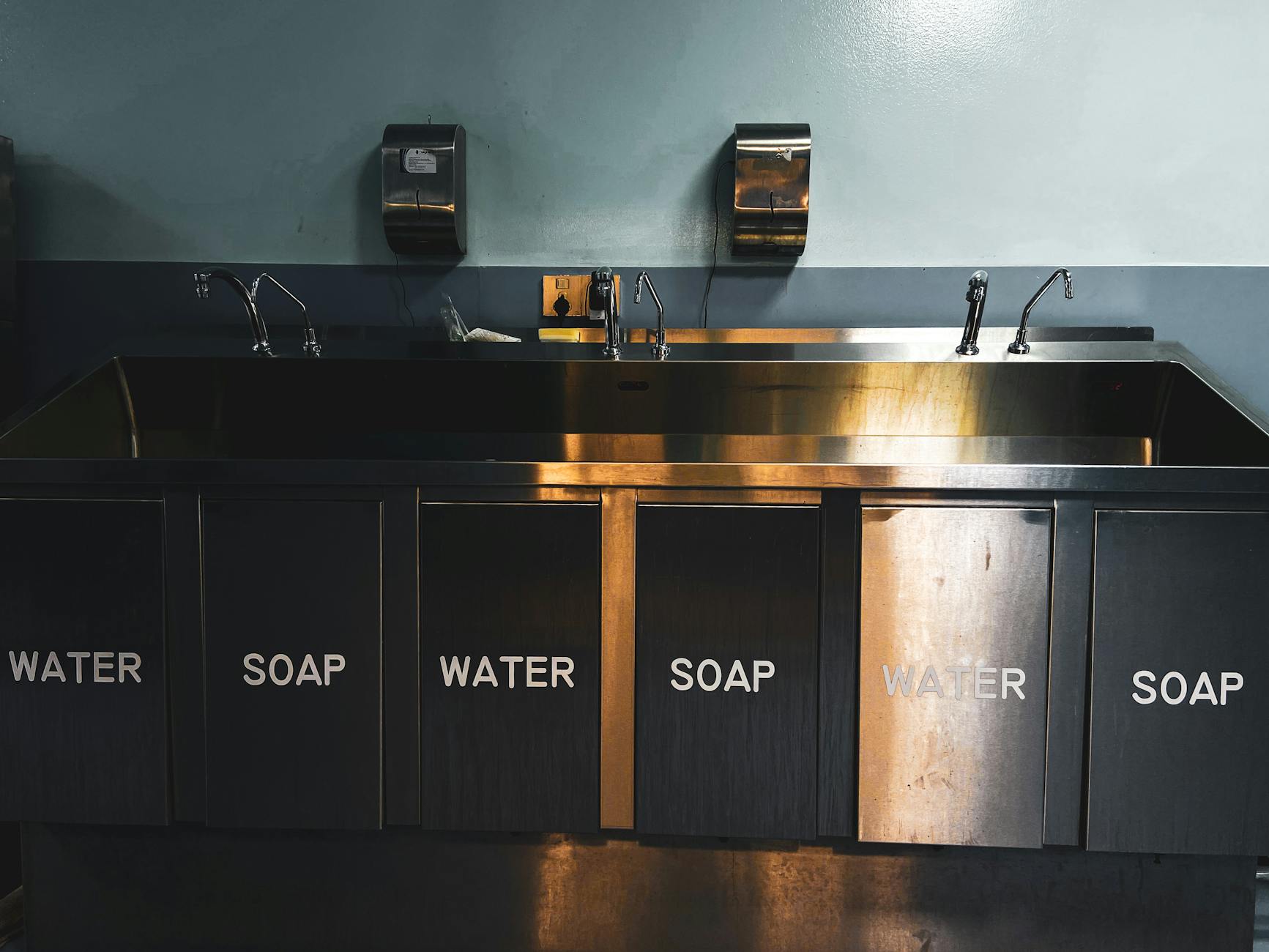 Three-compartment stainless steel sink in a commercial kitchen — drain trap and overflow are common secondary breeding sites for small flies in food-service operations